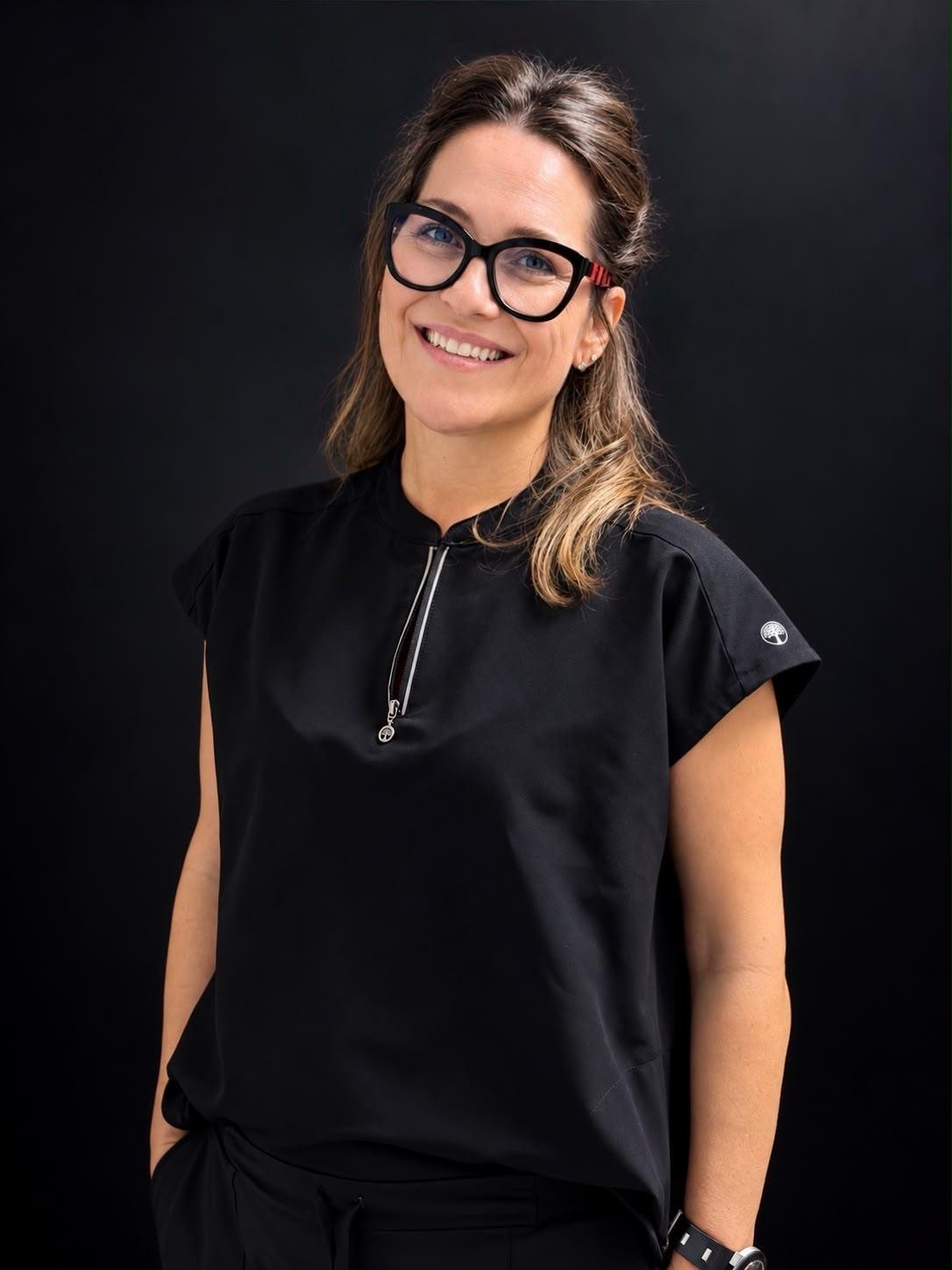 Retrato de la Dra. Nuria García, sonriendo, con gafas y uniforme negro.